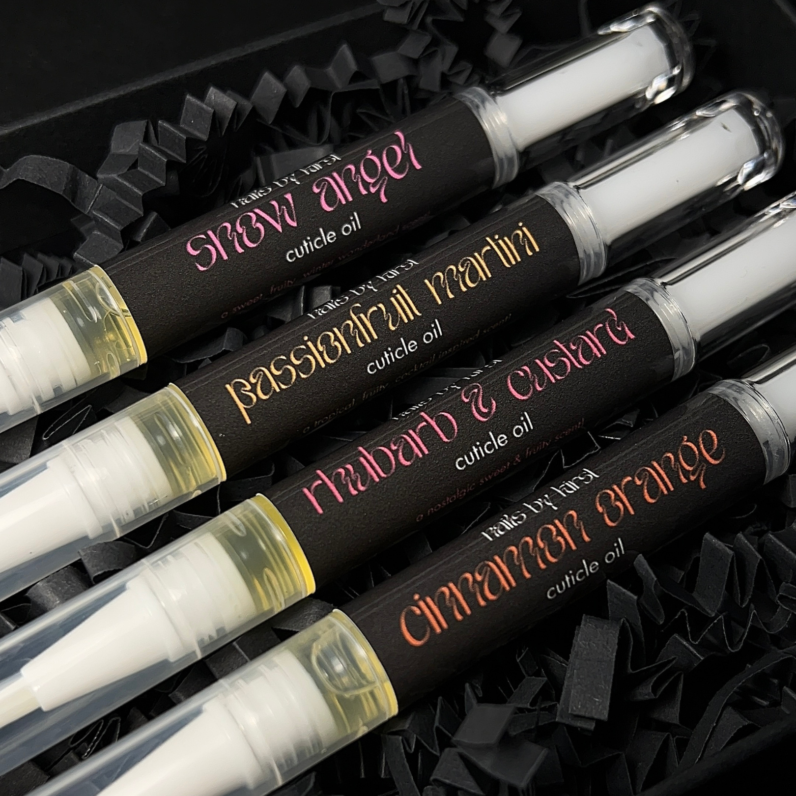 Set of cuticle oil bottles with colorful text on black labels.