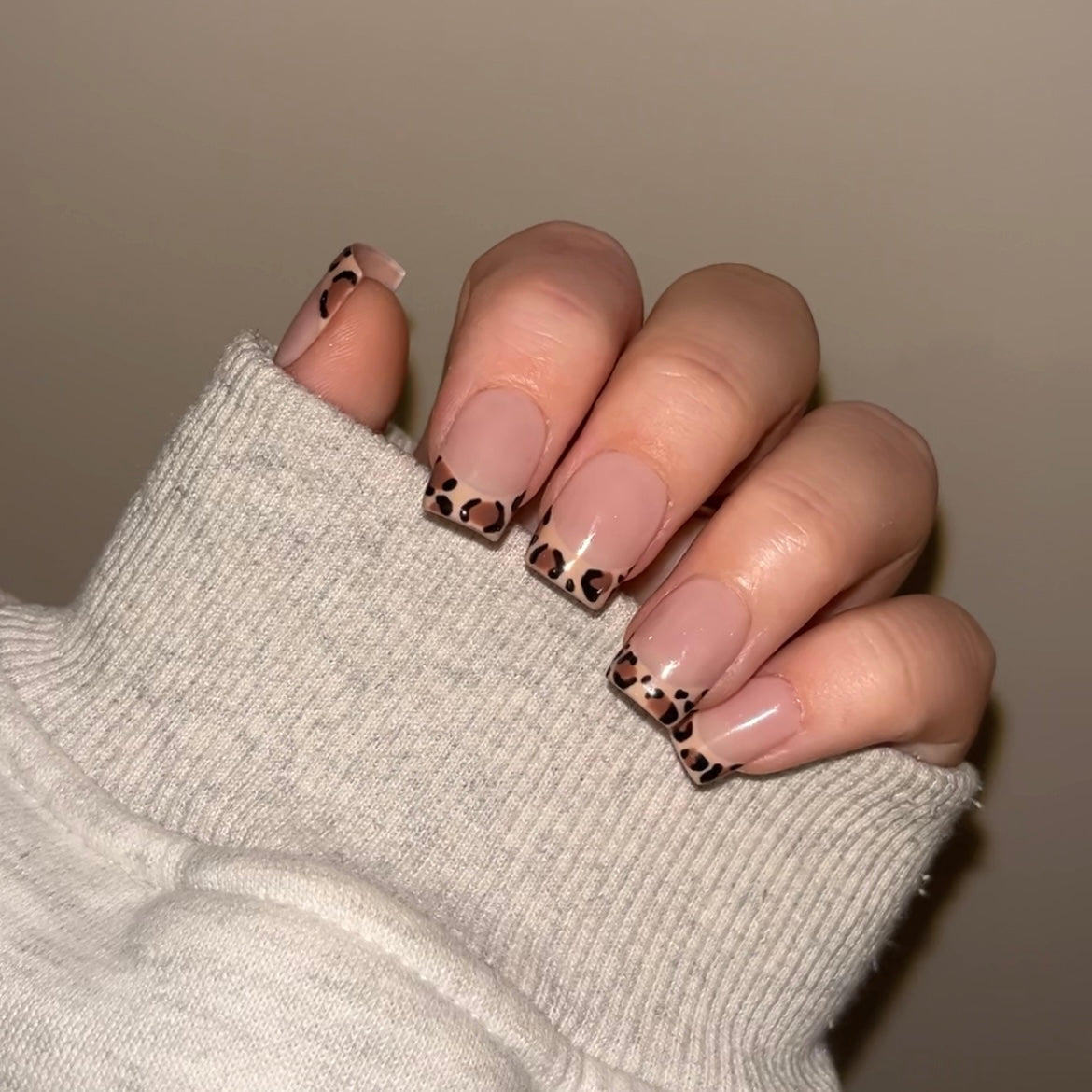 Hand wearing press on nails. The design is a beige french tip with leopard print on the french part.