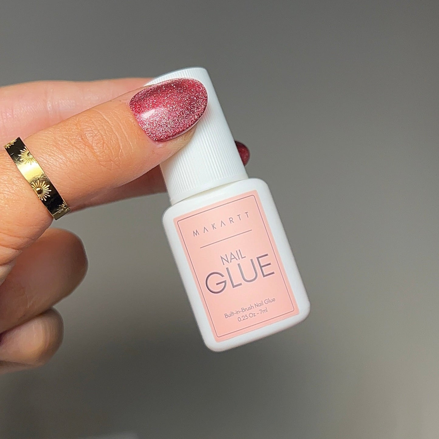 Hand holding a small bottle labeled 'nail GLUE' with a blurred background