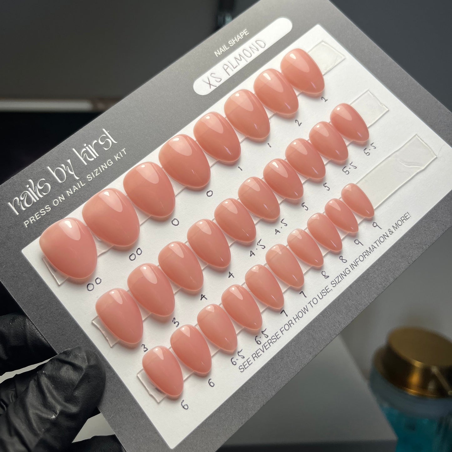 Set of nude-colored false nails on a display card held by a gloved hand.