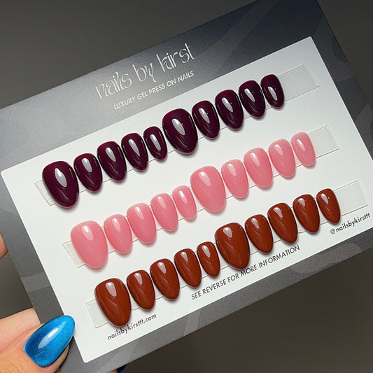 Set of nail art designs on a display card held by a hand with blue nail polish.