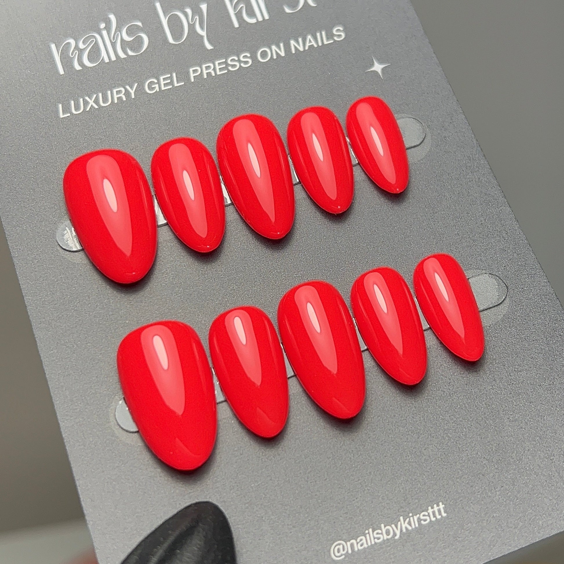Red press-on nails on a gray card held by a gloved hand.
