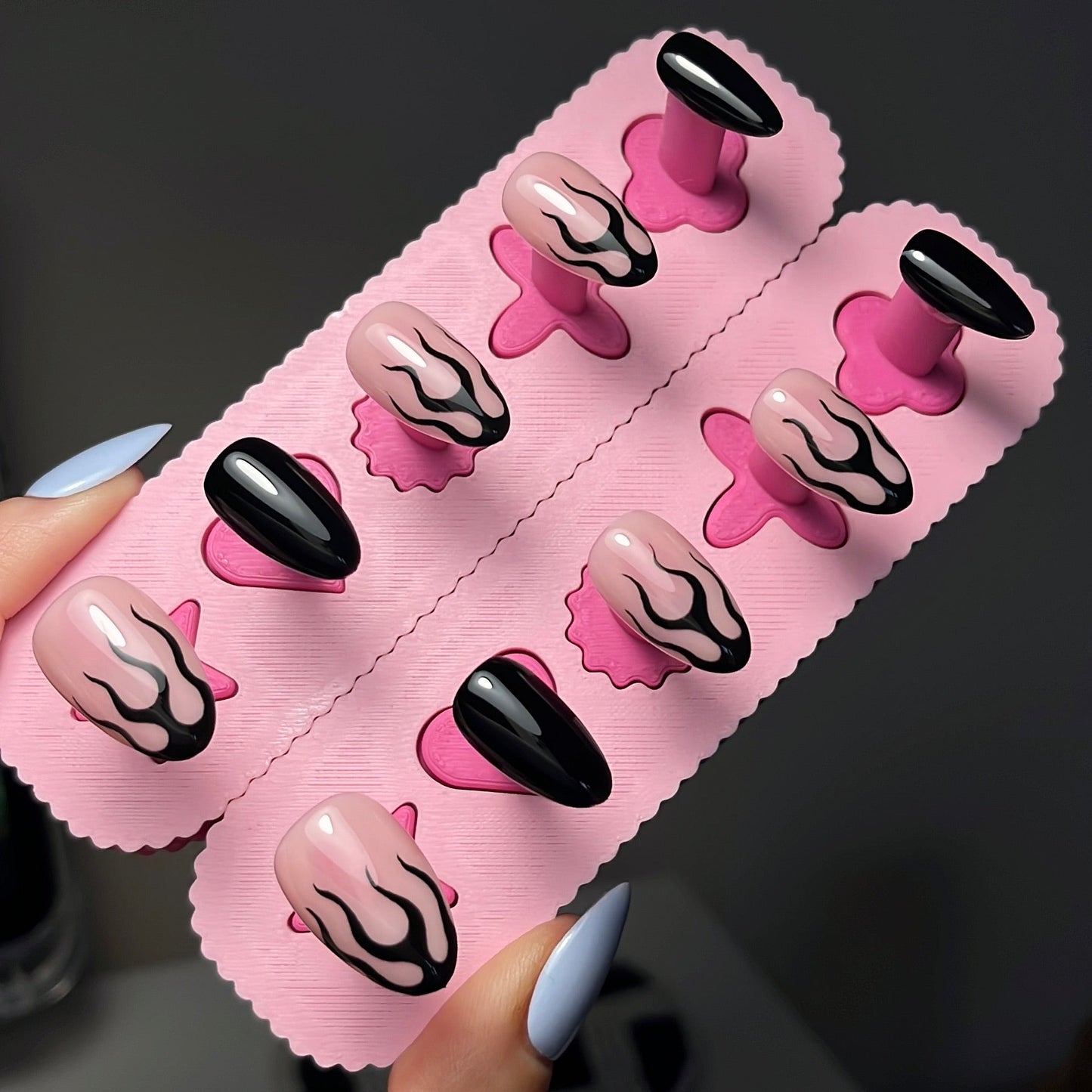 Pink nail art display with black and pink nails held by a hand against a dark background