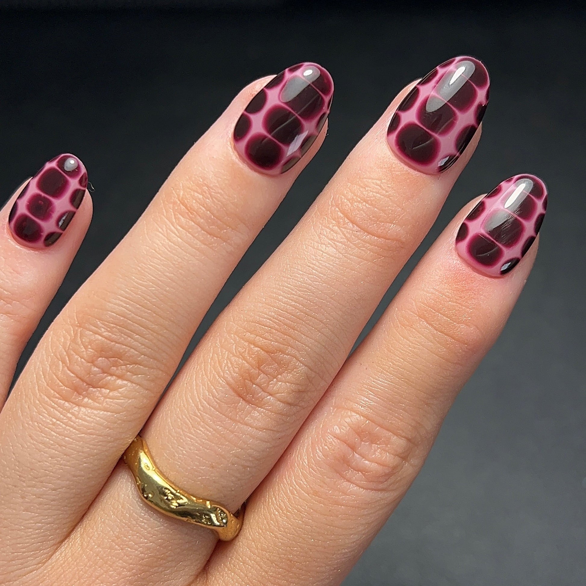 Hand with croc print nail design wearing a gold ring on a dark background