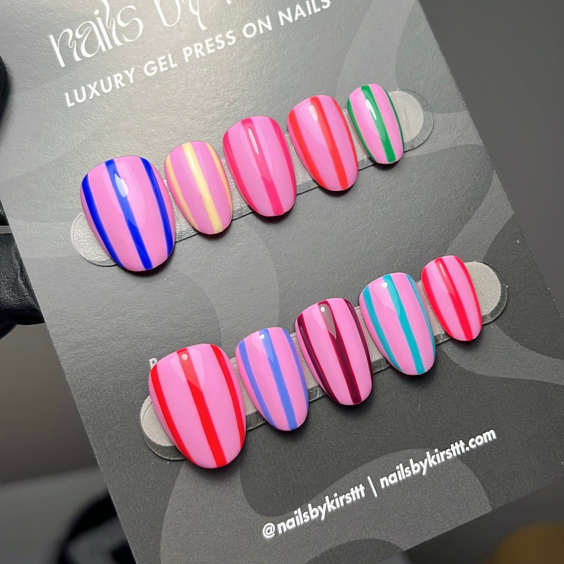 A set of artificial press-on nails displayed on a gray card labeled 'nails by kirst'. The nails feature stripe patterns.