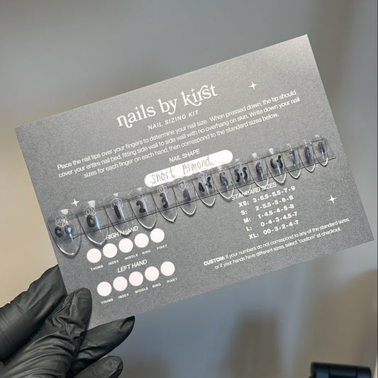 press on nail sizing kit on a backing card held by a person wearing black gloves with a blurred background